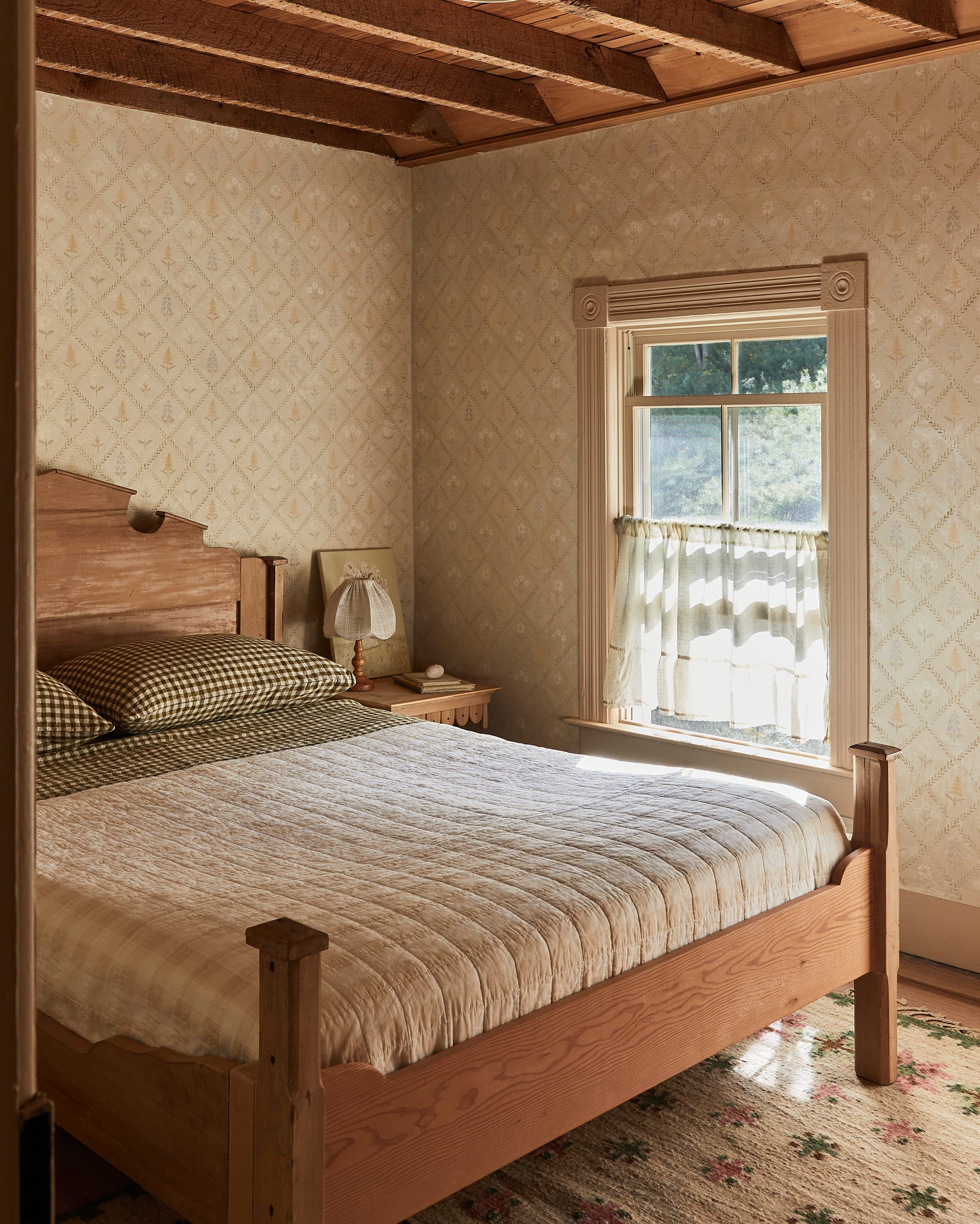 bedroom with aa bed with quilted bedding, wallpaper, a rug and a window