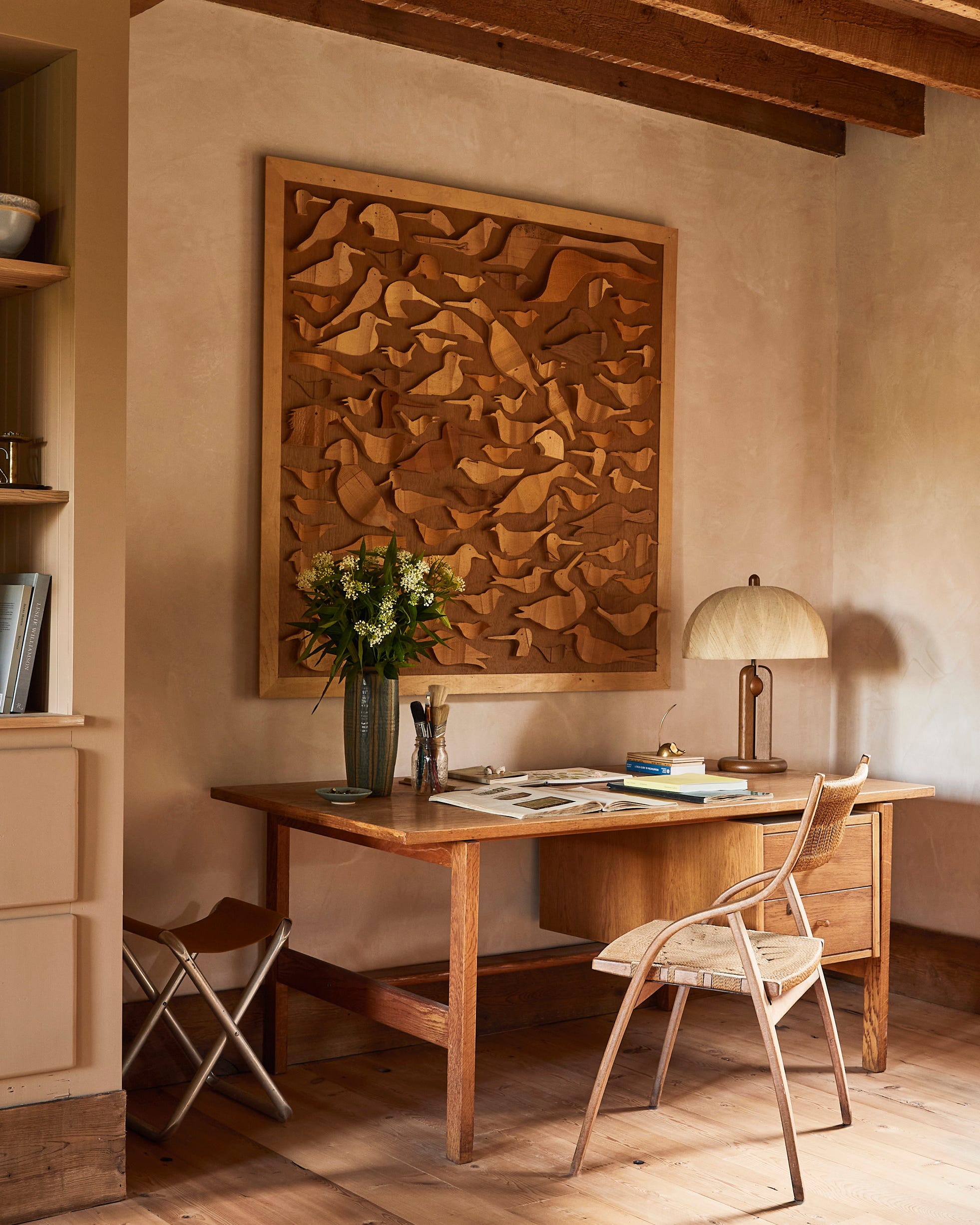 A cozy workspace featuring a wooden desk with a lamp a chair and artwork on the wall