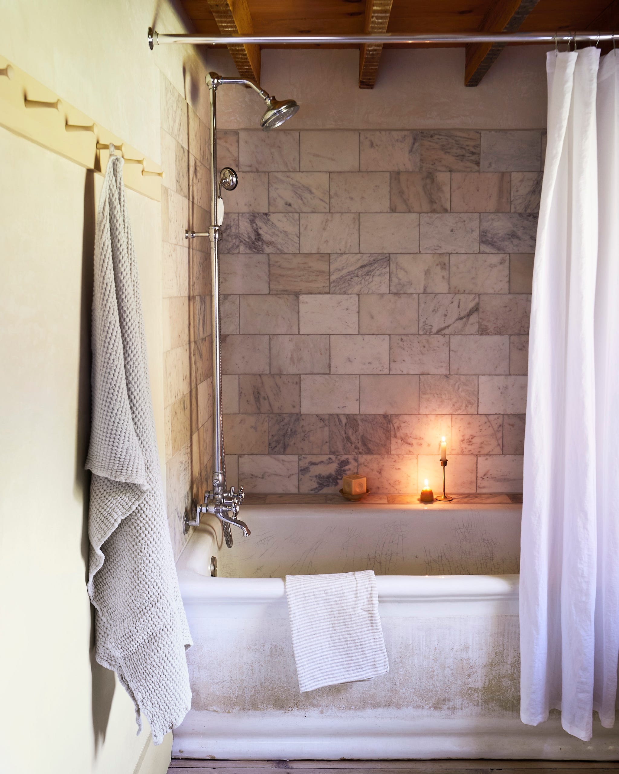 bathroom tub with marble tile around it and white shower curtain