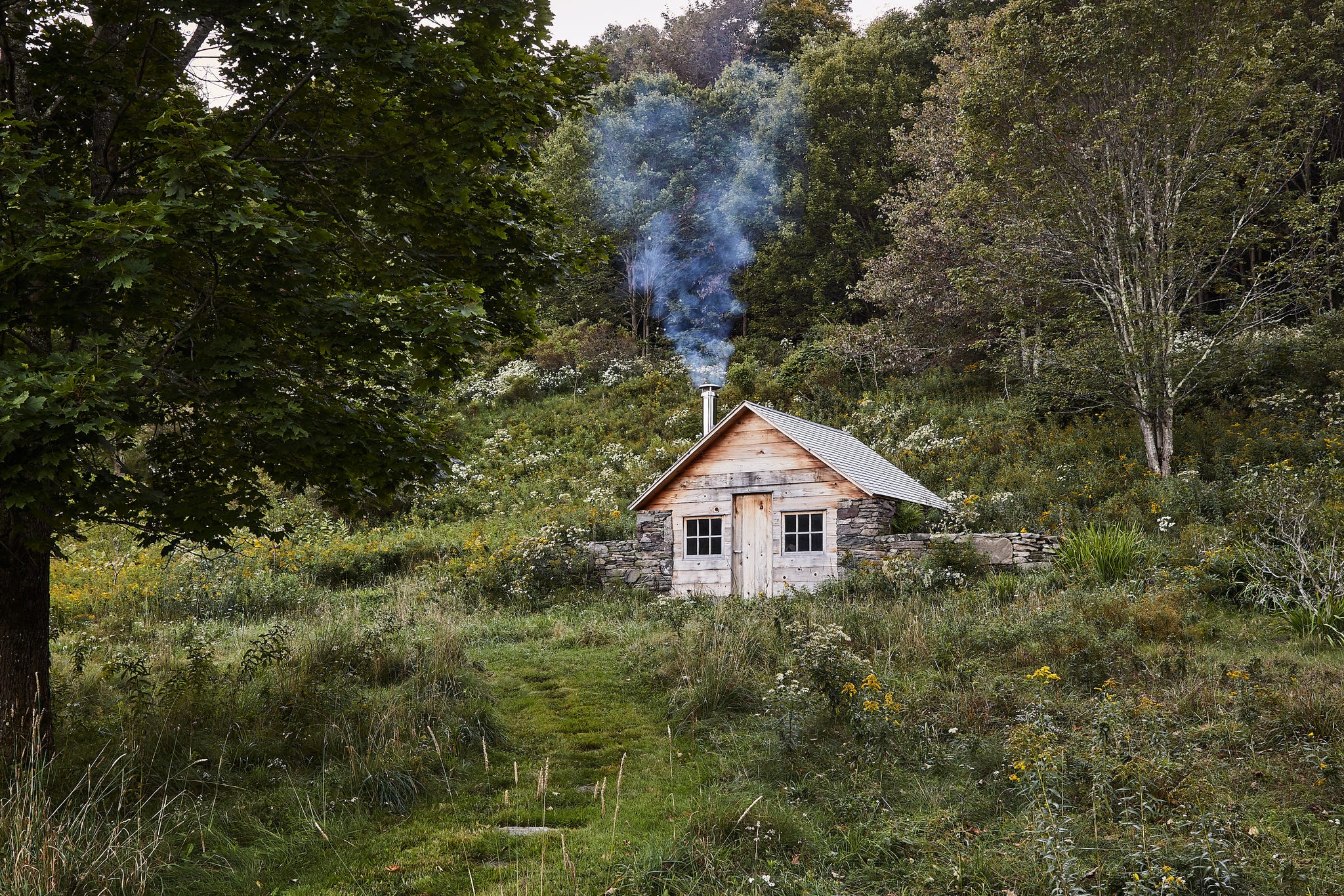 sauna building with wood siding and stone walls surrounded by trees and grass